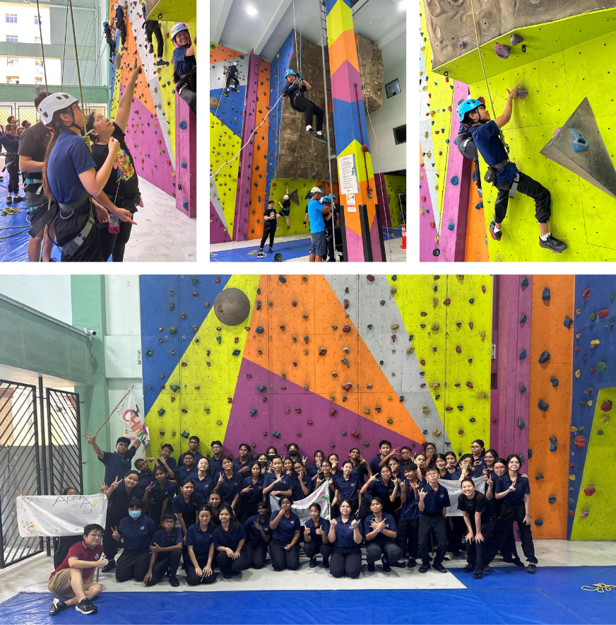 A large group of students in dark uniforms pose in front of colorful indoor climbing walls, with action shots of climbers above.