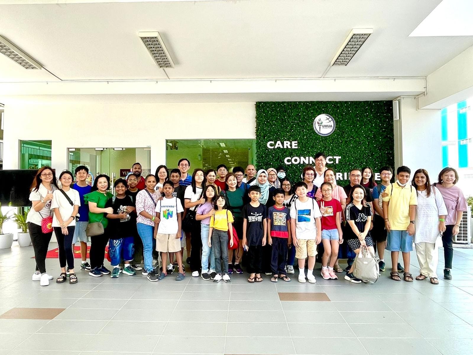A large group of adults and children posing together indoors in front of a green wall with the words Care Connect.
