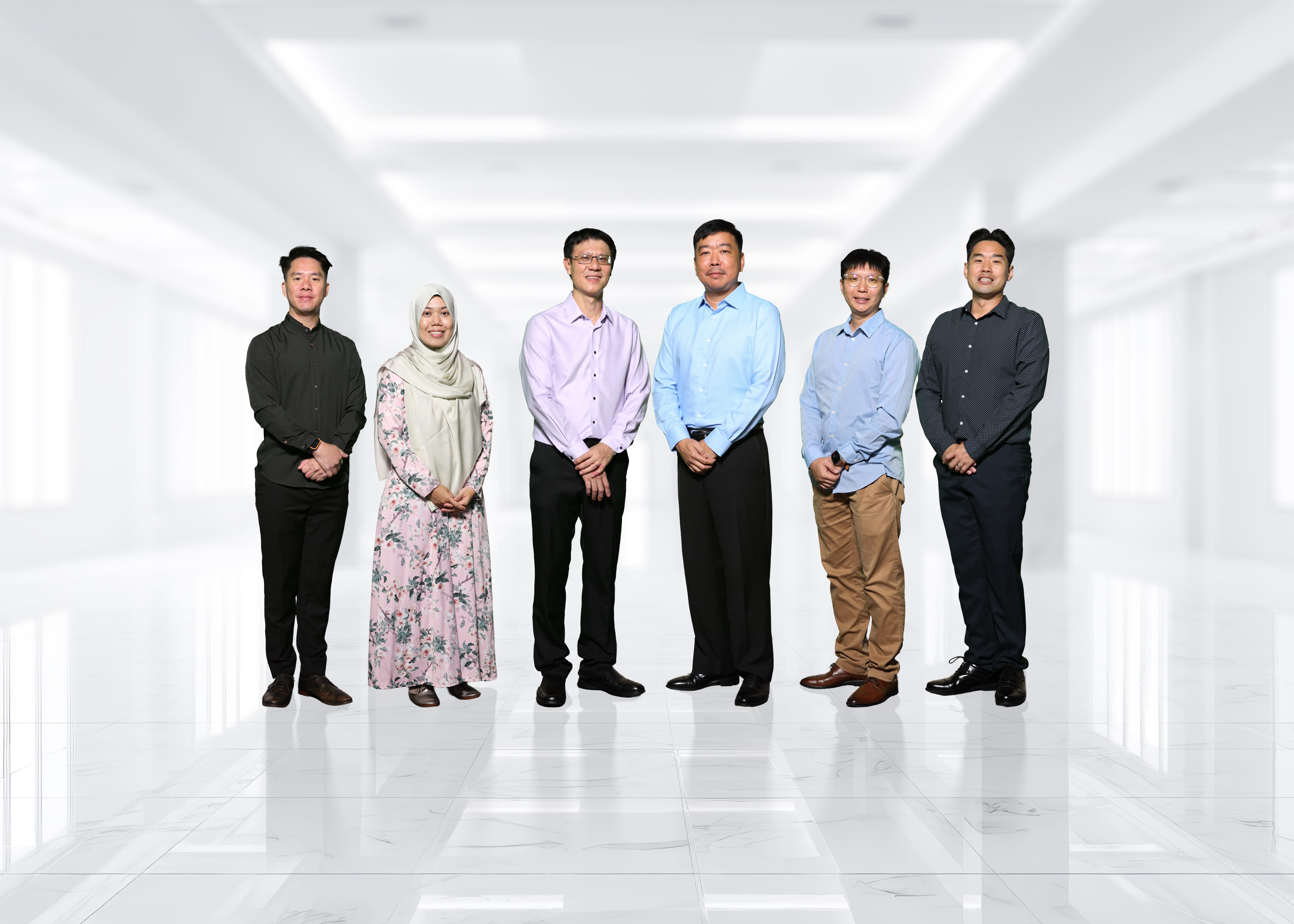 Six adults standing in a row in a bright hallway; one wears a hijab and floral dress, others in shirts.