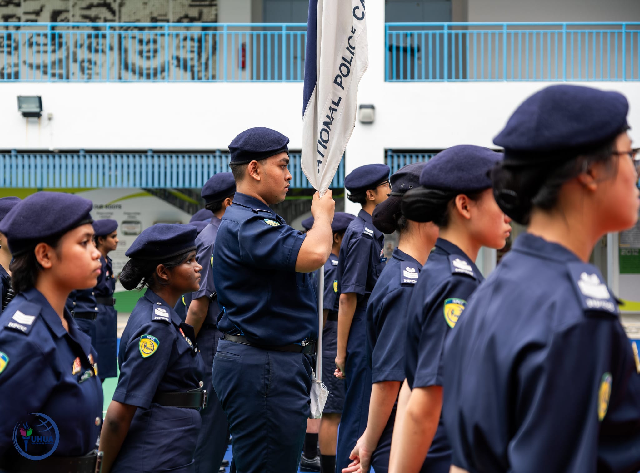 A group of National Police Cadet Corps members in navy uniforms and berets standing in formation, one holding a flag.