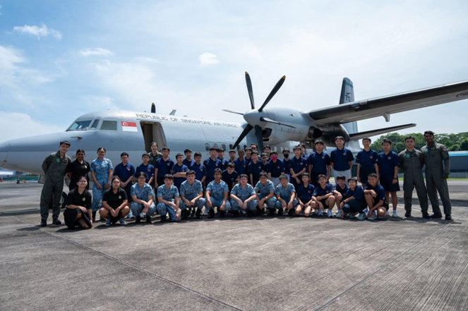 A large group of young people in uniform pose in front of a Republic of Singapore Air Force aircraft on a tarmac.