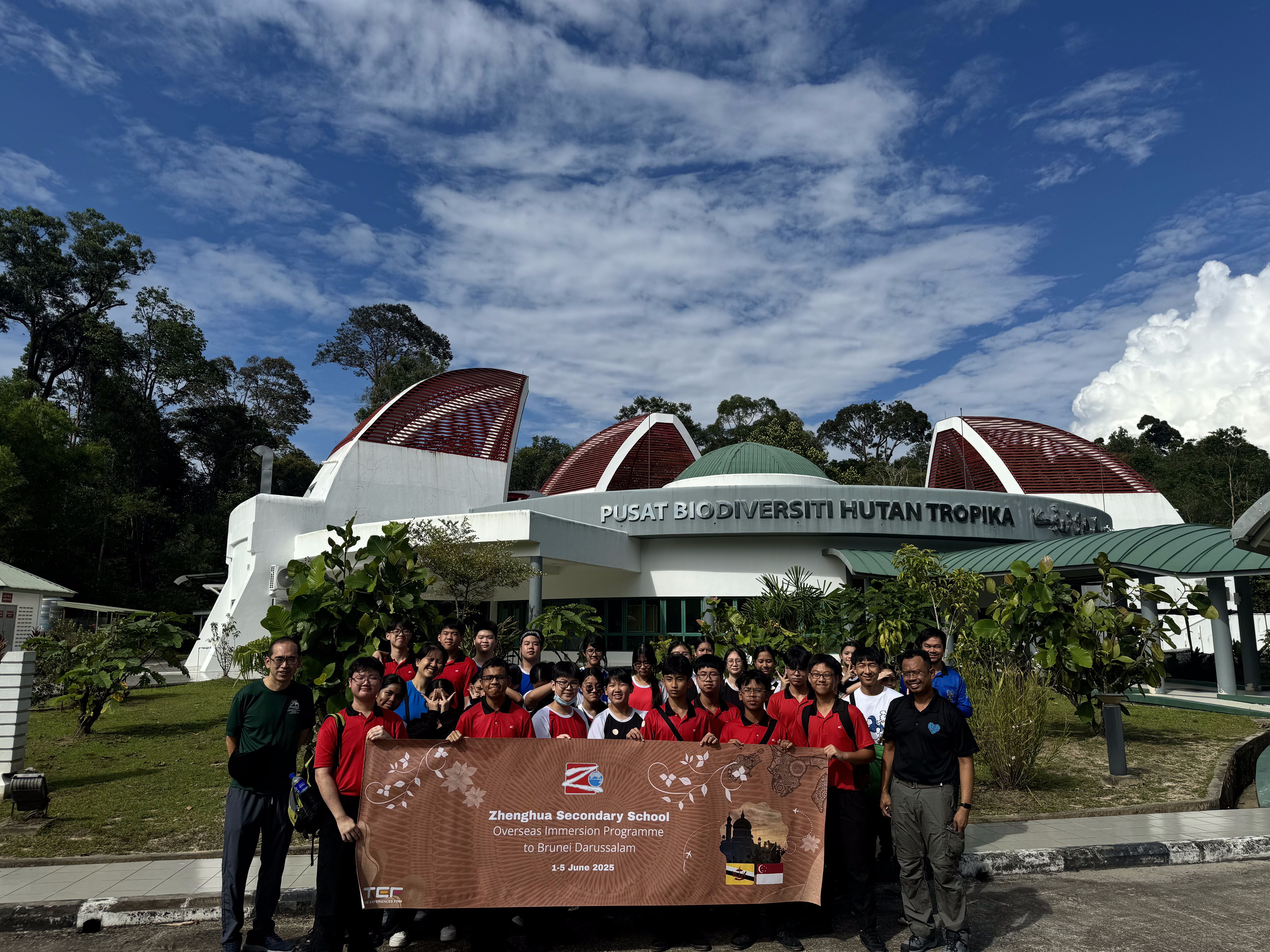 A group of students in red shirts hold a Zhenghua Secondary School banner outside Pusat Biodiversiti Hutan Tropika in Brunei.
