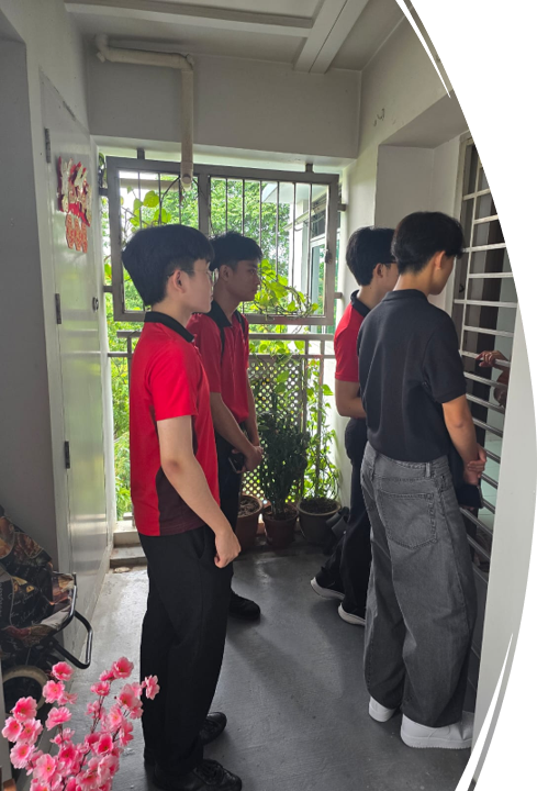 Four young males in red and dark polo shirts stand in a narrow corridor near a barred window with plants.