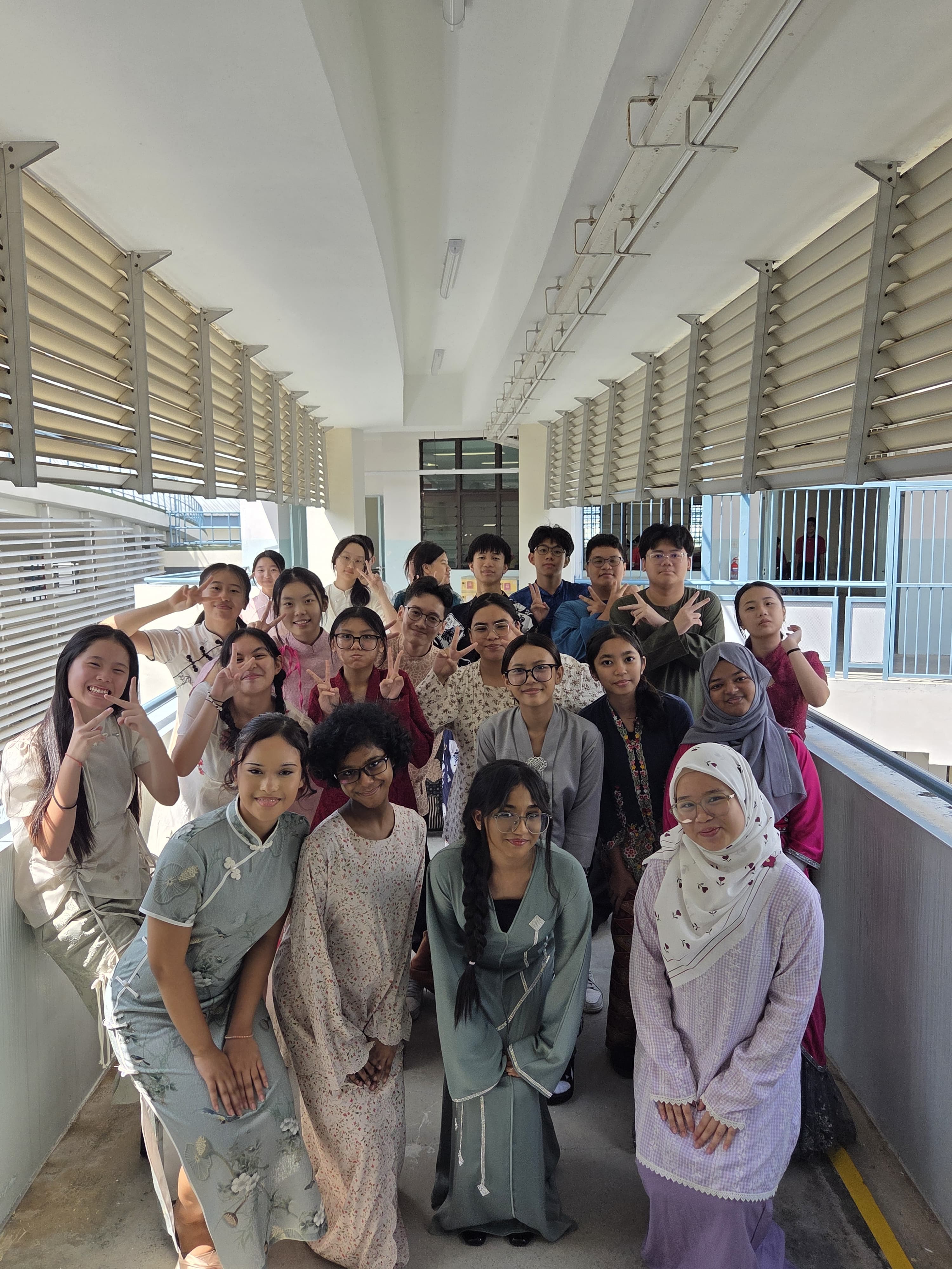 A large group of young people in traditional cultural attire posing together in a bright indoor corridor.