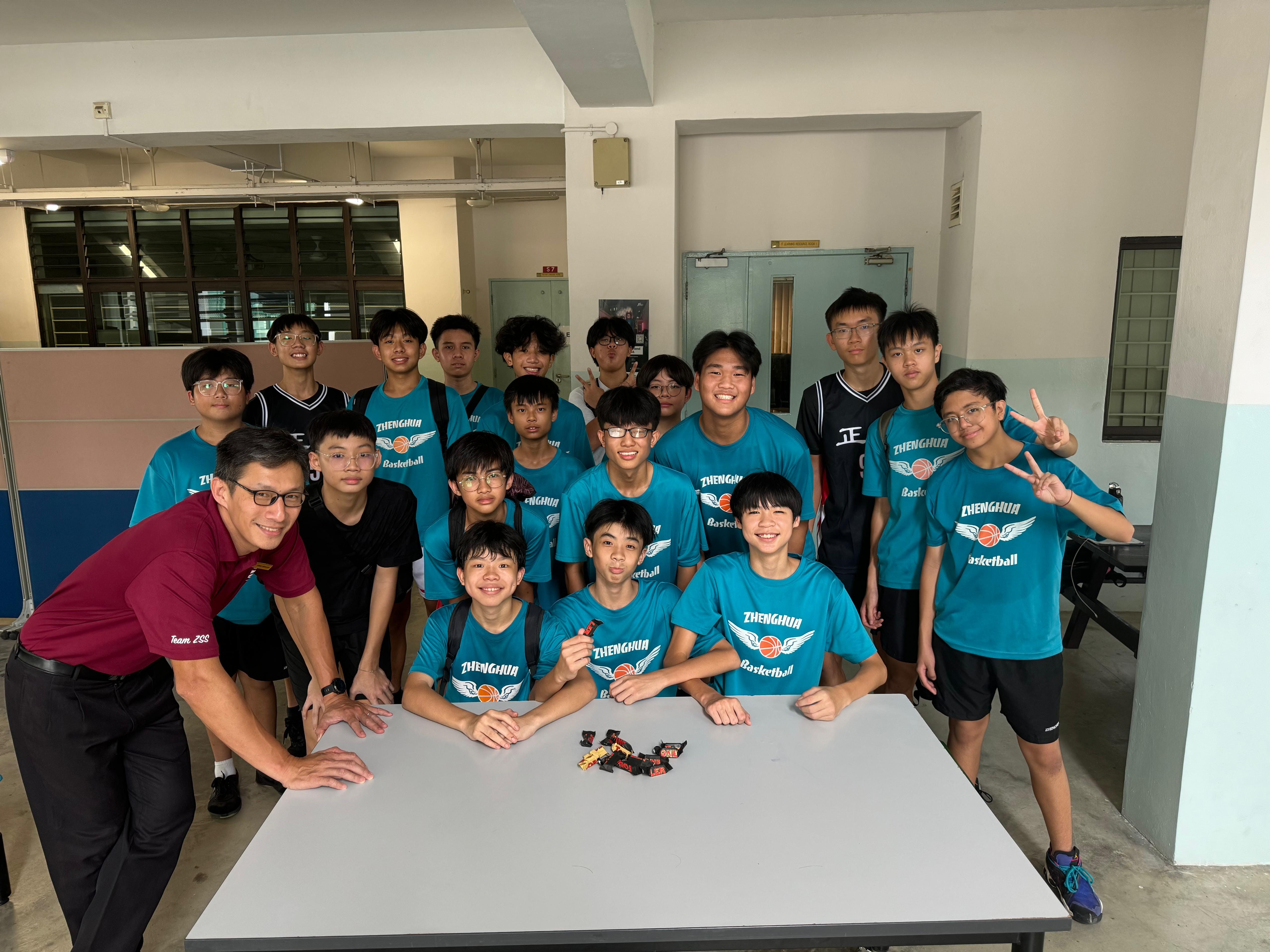 A group of teenage boys in teal Zhenghua Basketball shirts pose with an adult male indoors.