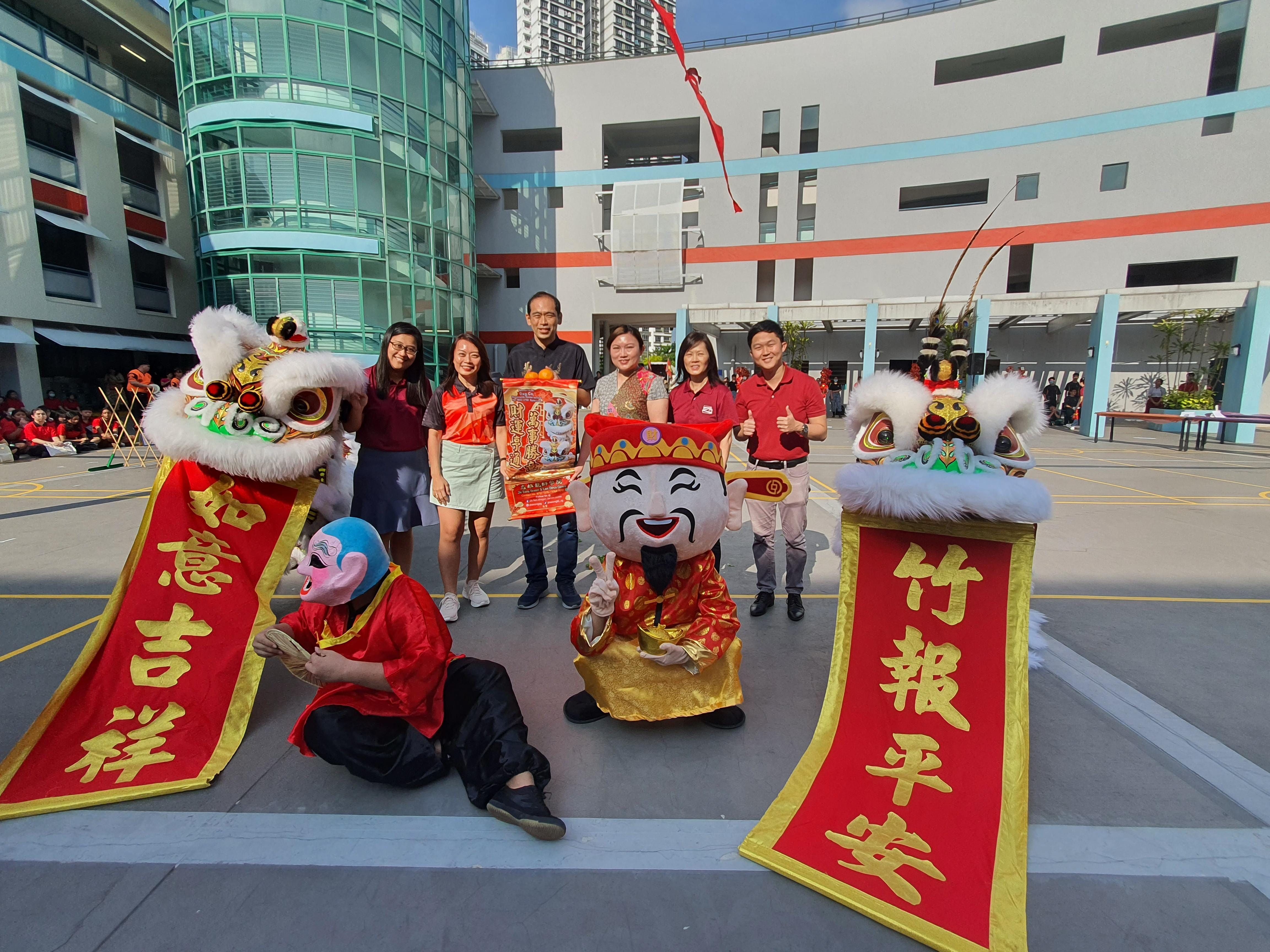 Group poses with lion dance costumes and a Chinese God of Wealth mascot holding red banners with gold characters.