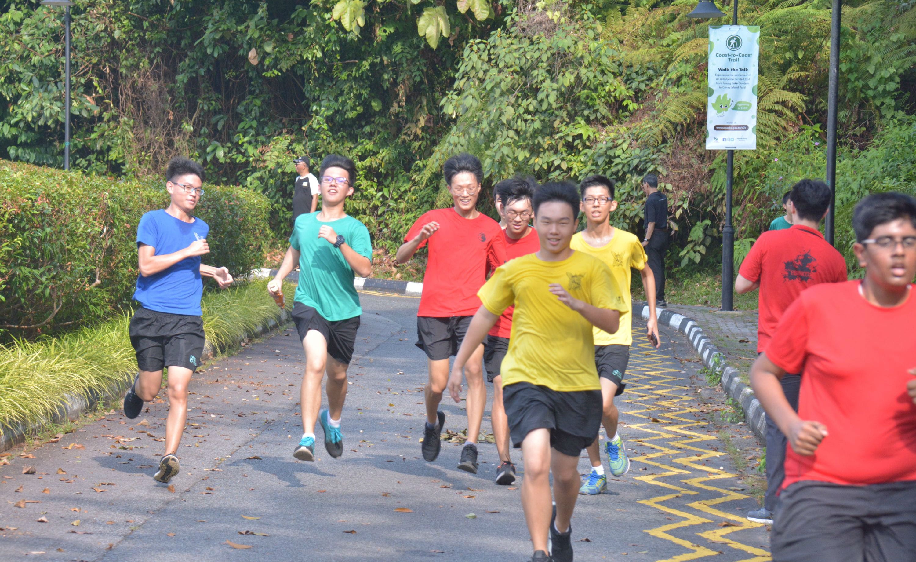 A group of young men in colorful shirts running along a tree-lined road near a Coast-to-Coast Trail sign.