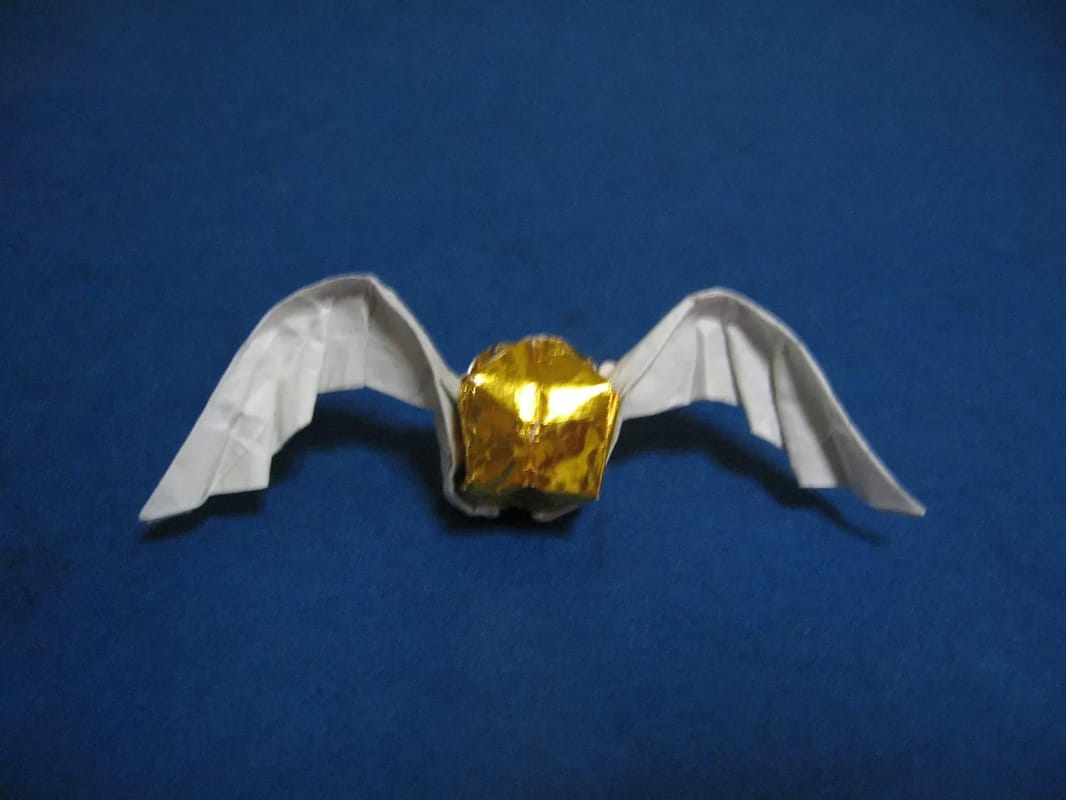A gold foil ball with white paper origami wings spread out, resting on a blue surface.
