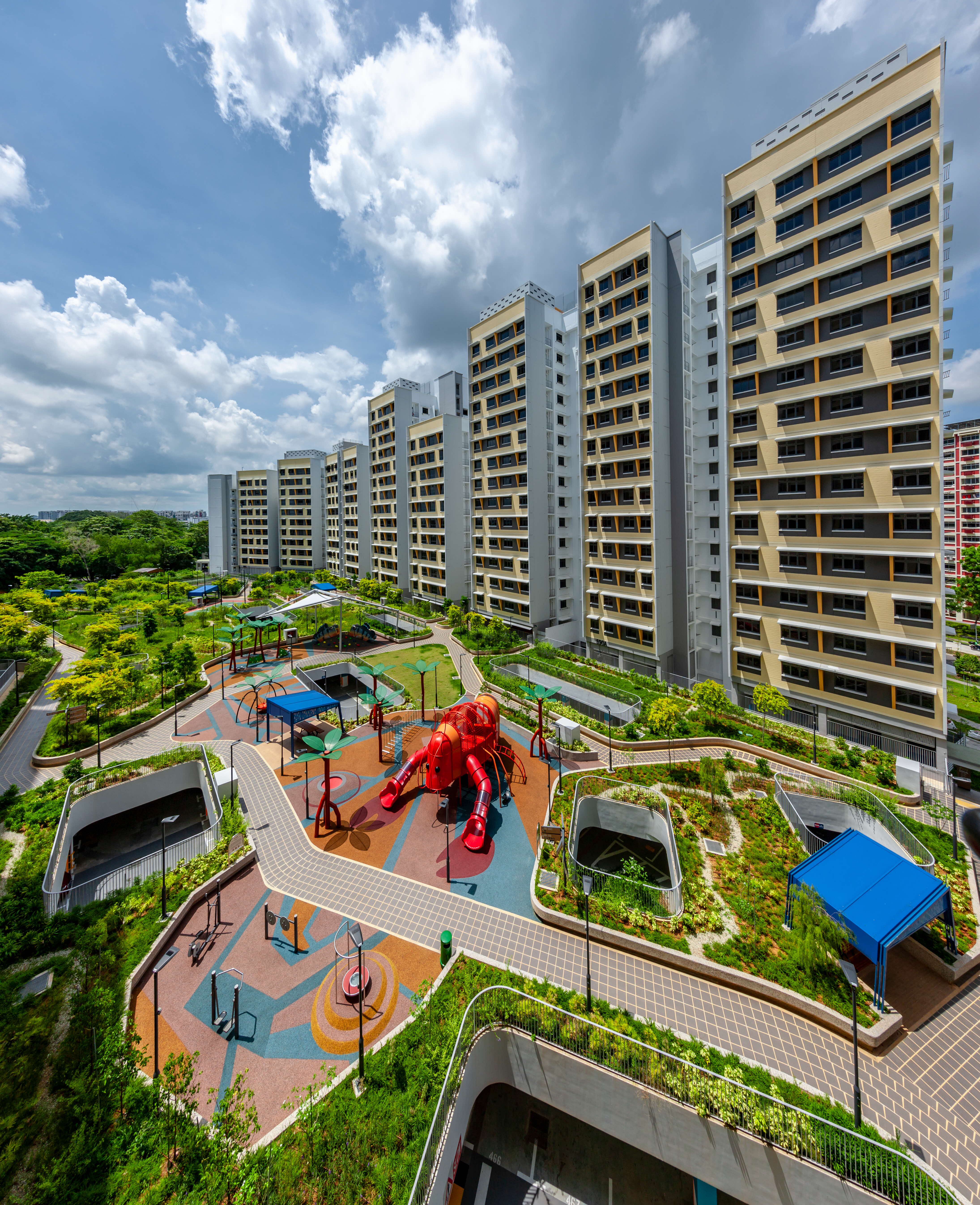 Tall apartment blocks beside a landscaped courtyard with paths and a playground featuring a large red slide.