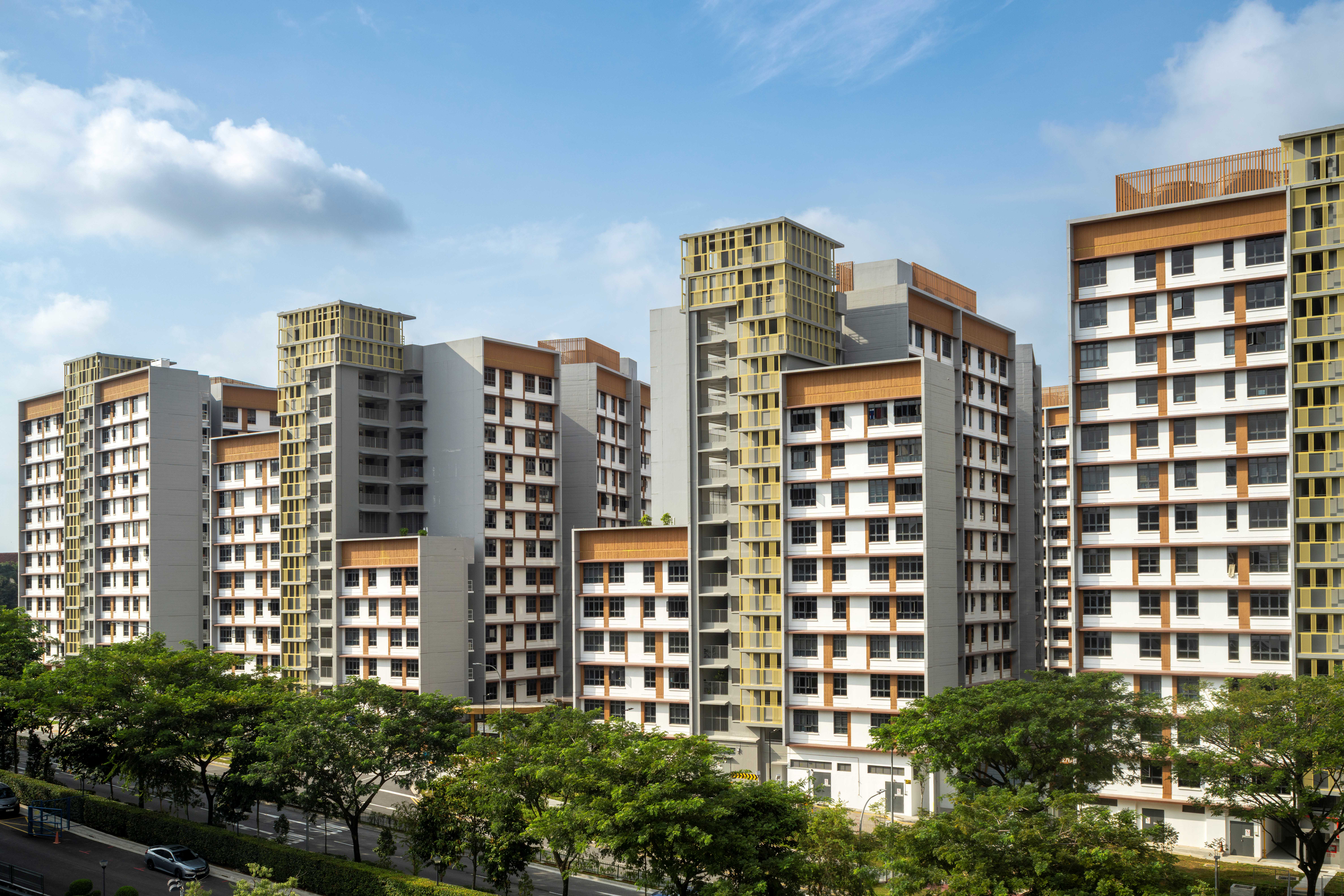 Cluster of modern high-rise apartments with balconies, above trees along a street under a blue sky
