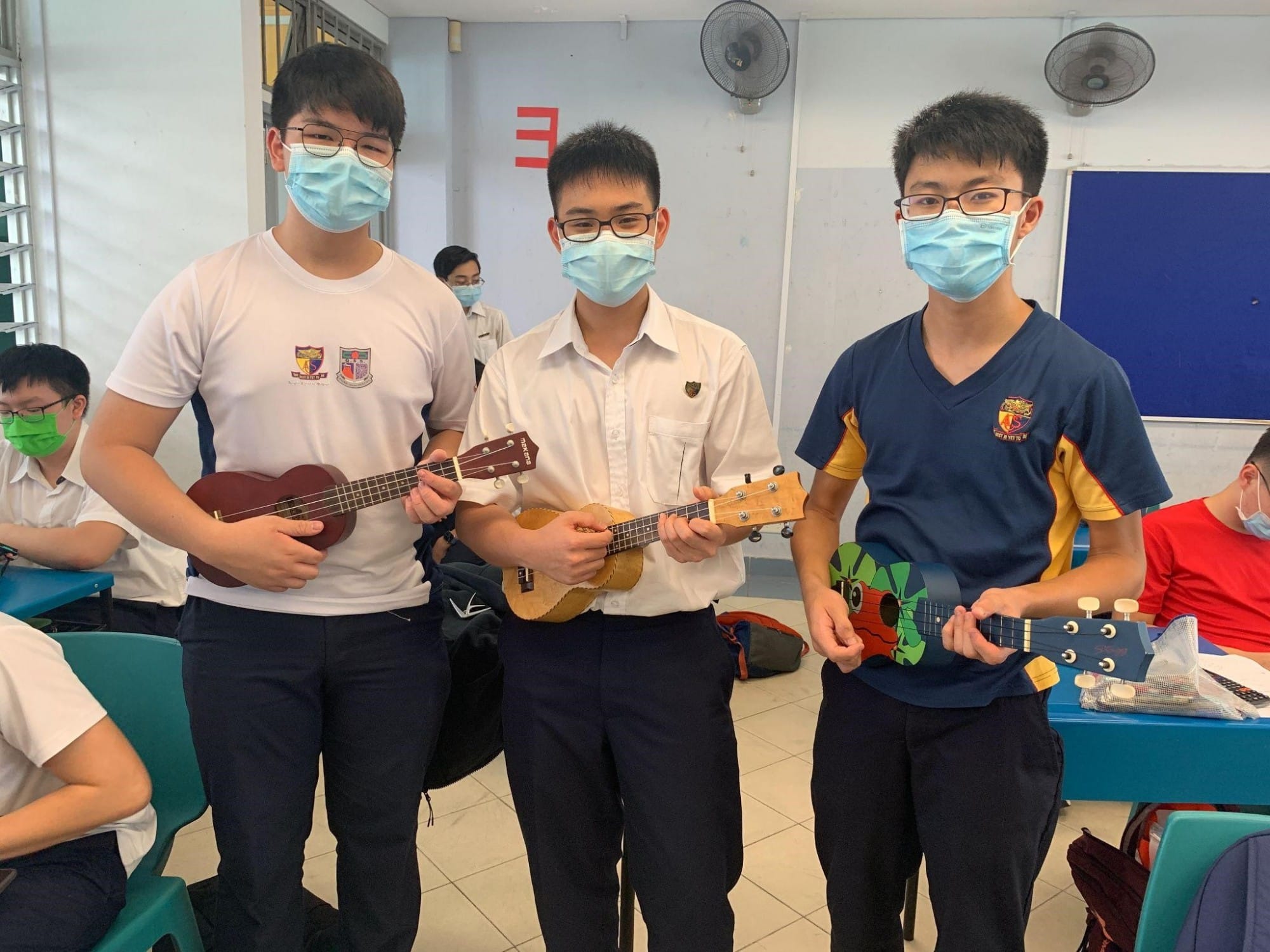 Three students hold ukuleles in a classroom.