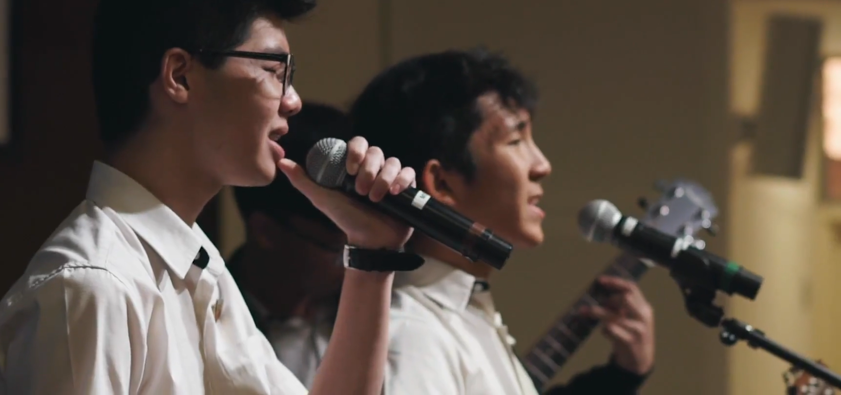 Two students performing, one singing into a handheld microphone and another at a mic stand.