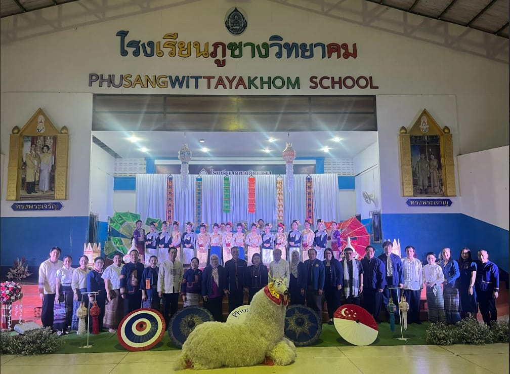 Group of people posing in front of Phusangwittayakhom School stage with traditional Thai costumes and decorations.