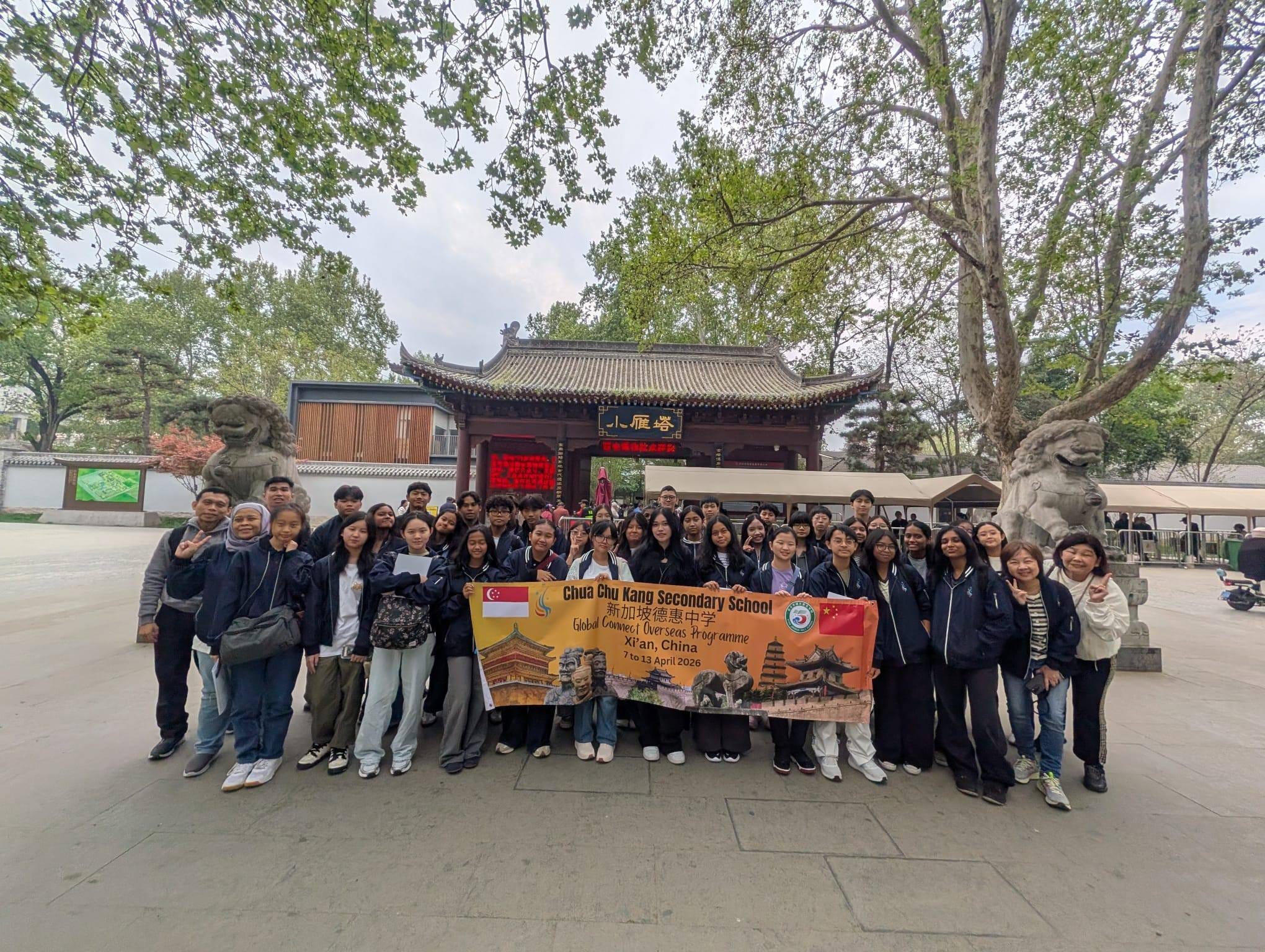 A large group of people pose with a banner in front of a temple