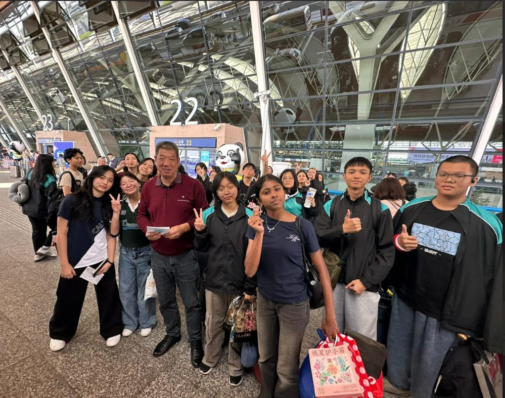 A large group of students and an adult man pose together at a Chinese airport terminal near gate 22.