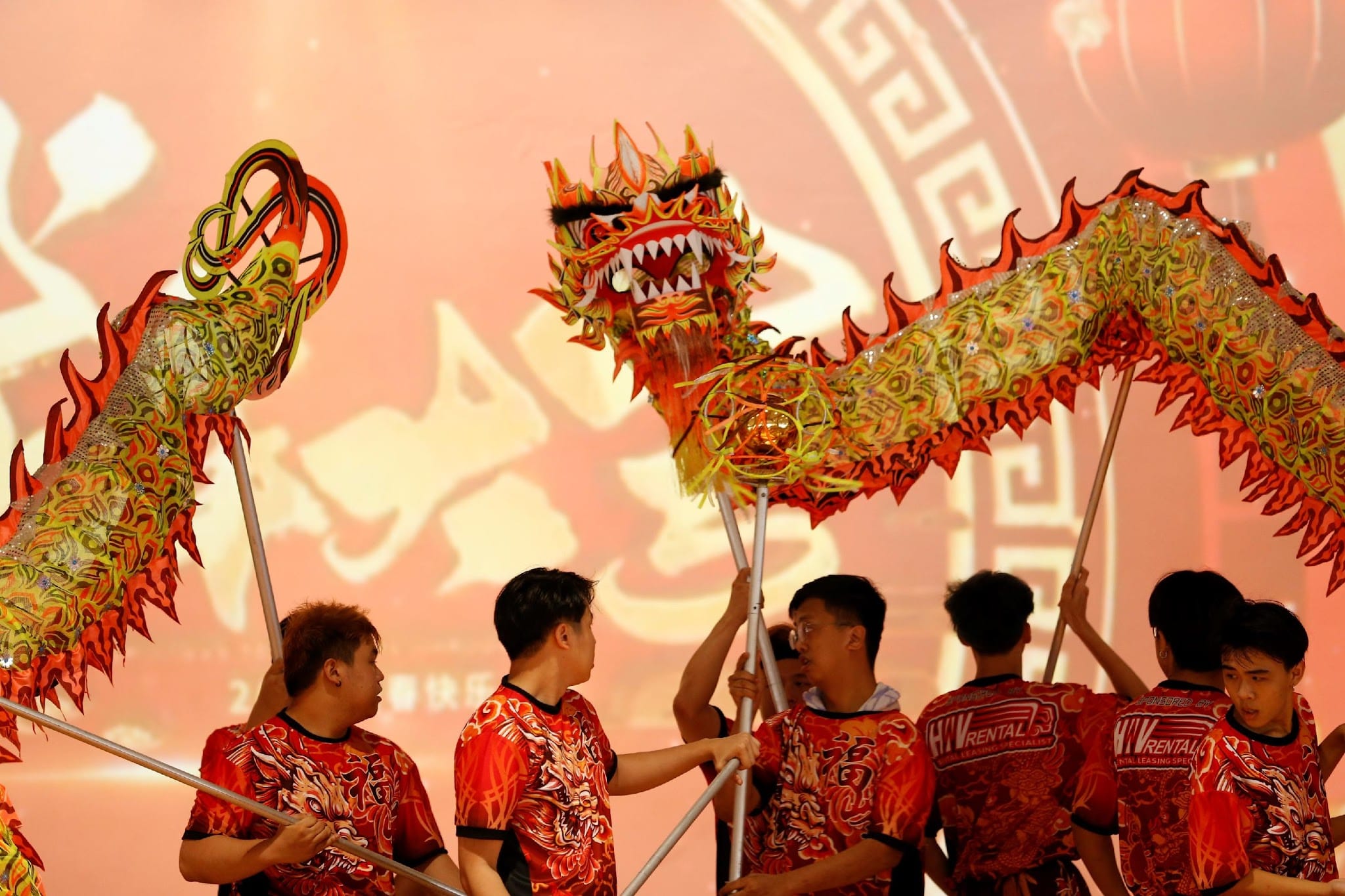 Performers in red shirts hold poles to animate a colorful red and gold dragon during a traditional dragon dance.