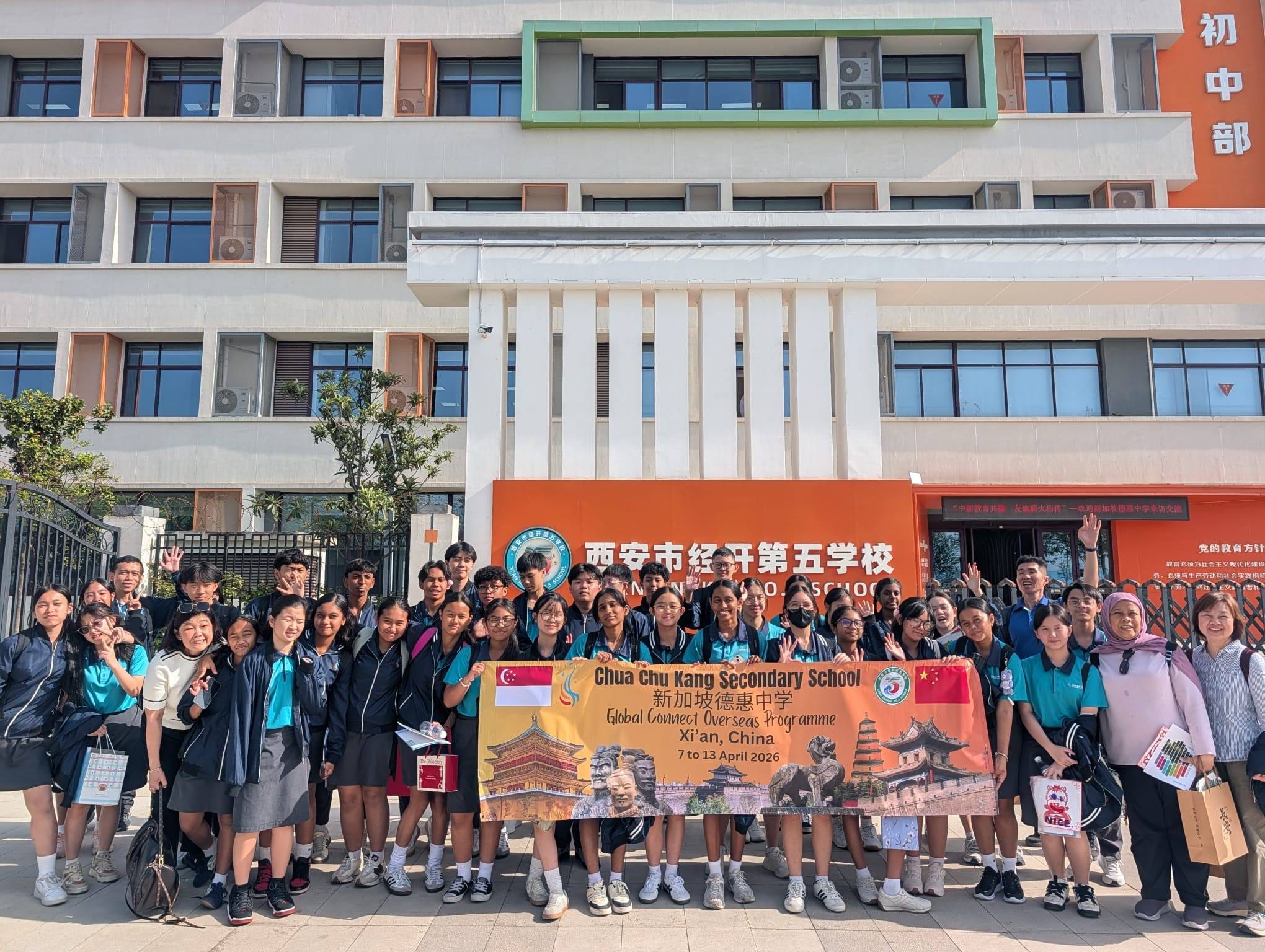 a large group of people posing with a banner in front of a school building