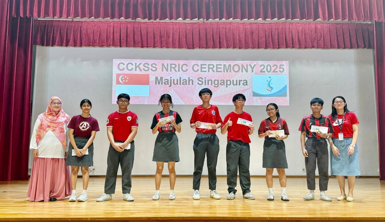 Eight people stand on a stage in front of a banner reading CCKSS NRIC Ceremony 2025 Majulah Singapura.
