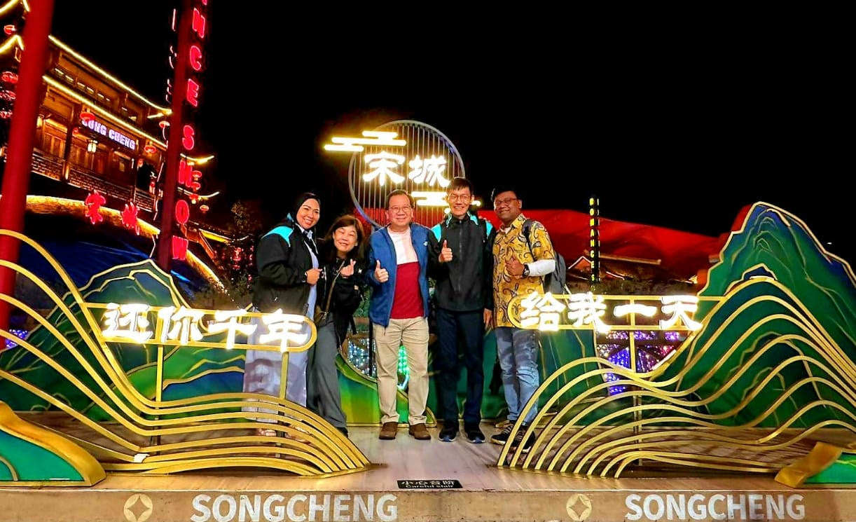 Five people pose at night in front of a lit Songcheng sign with Chinese characters and colorful decorations.