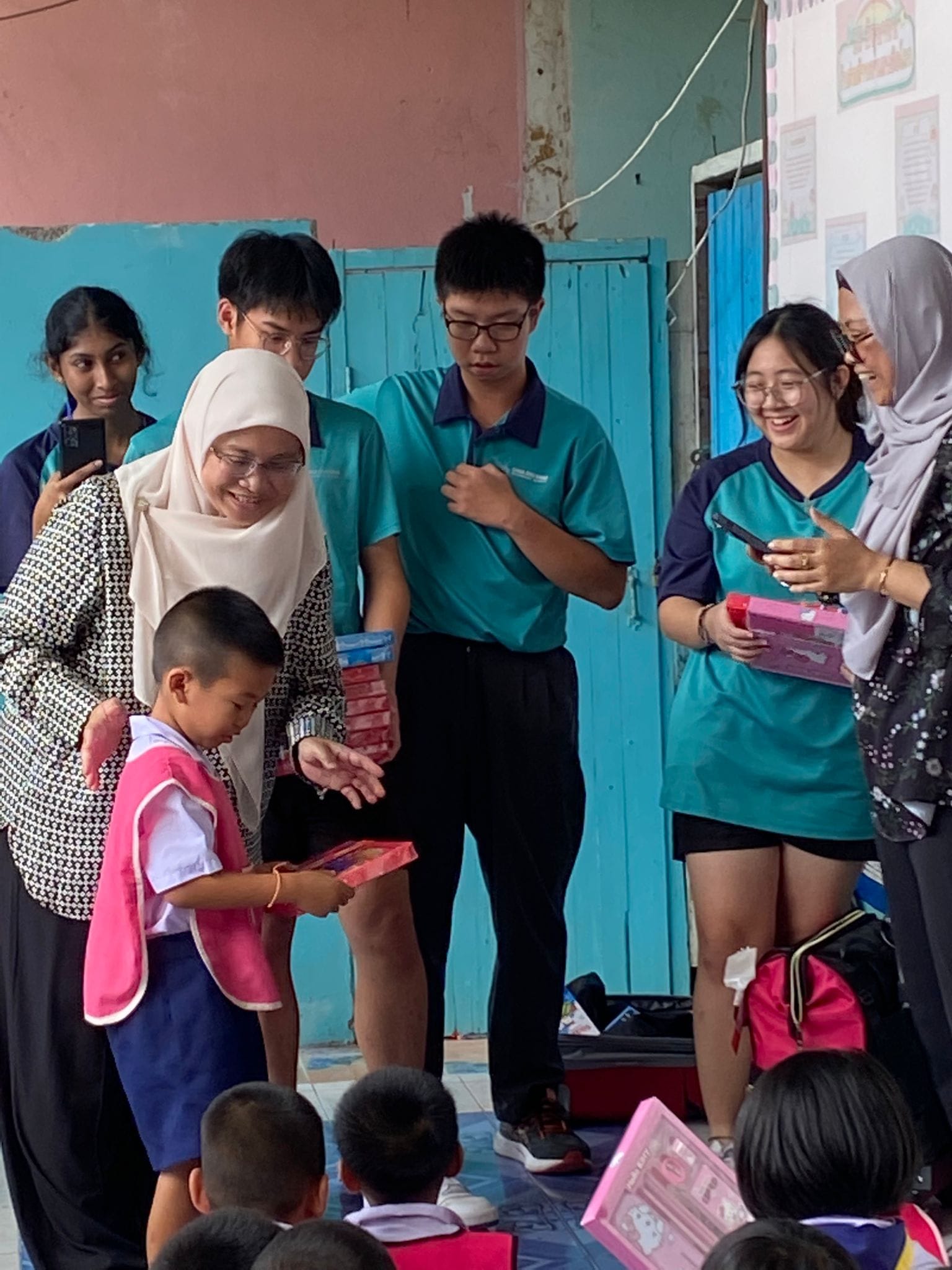 2 women in hijab and 4 students distribute gifts to little children.