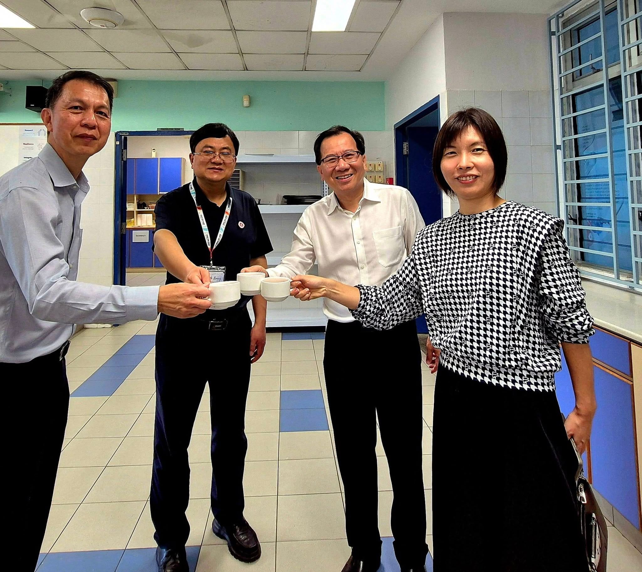 Four people smiling and toasting with small white cups in an indoor tiled room.