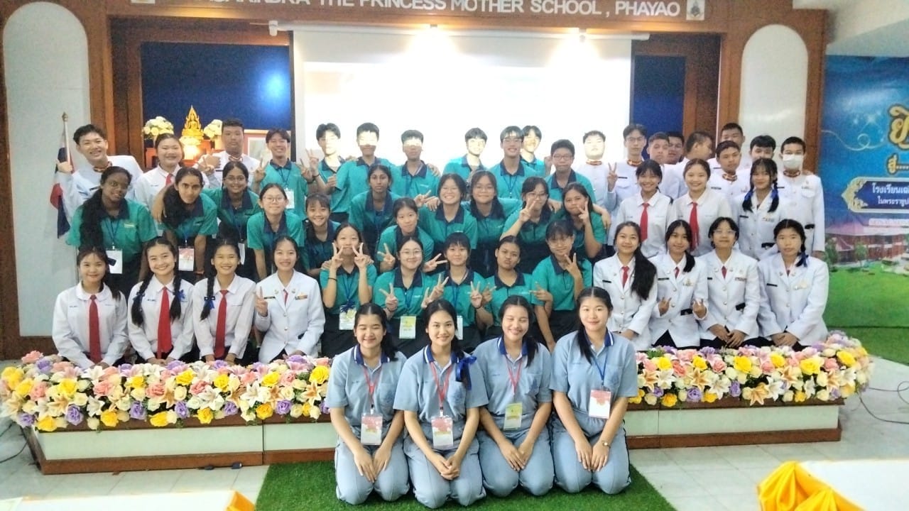 A large group of students in uniforms pose together in front of a sign reading Princess Mother School, Phayao.