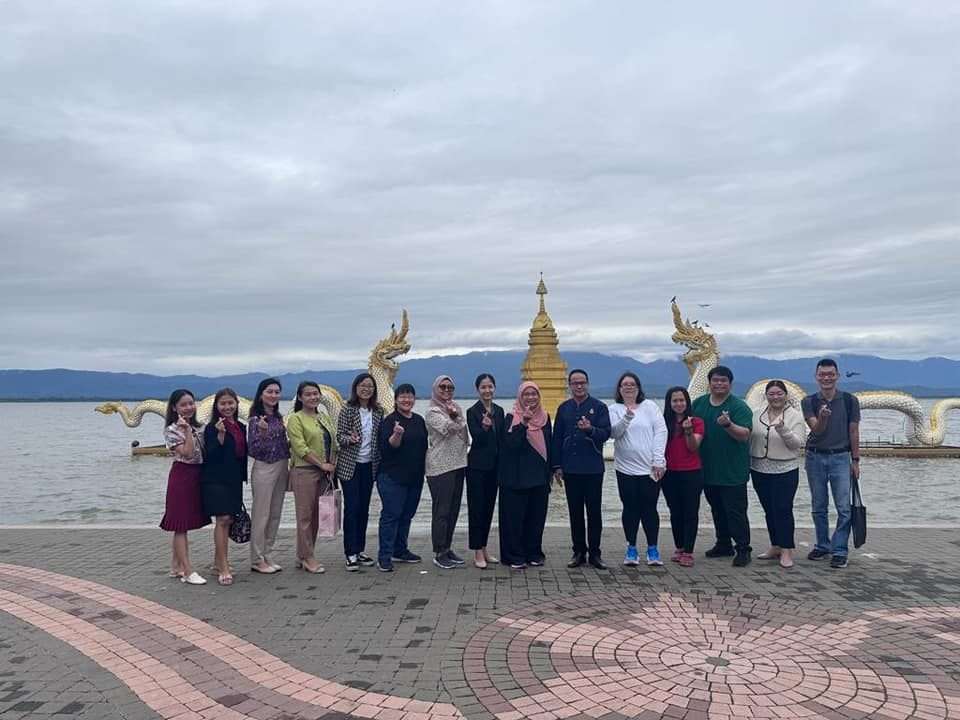 A group of about 13 people posing by a lakeside with a golden pagoda and dragon statues behind them.