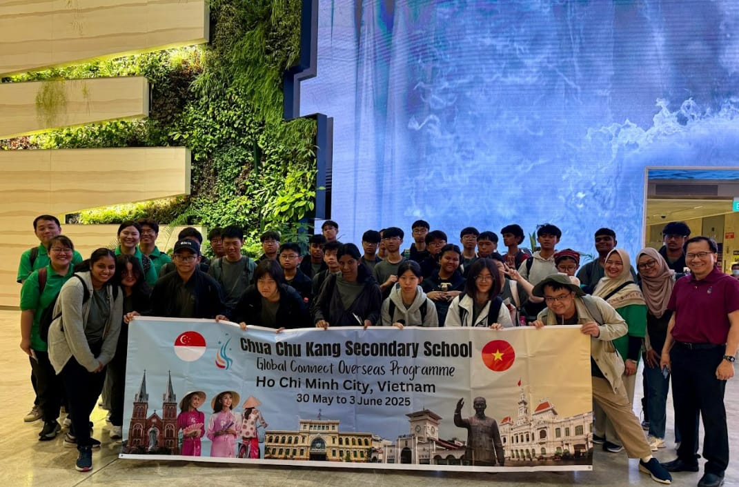 Group of students and teachers holding a Chua Chu Kang Secondary School Vietnam programme banner, posing indoors.