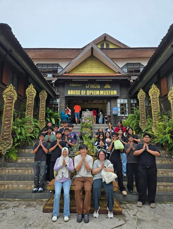 A group of students posing with prayer hands in front of the House of Opium Museum building in Thailand.