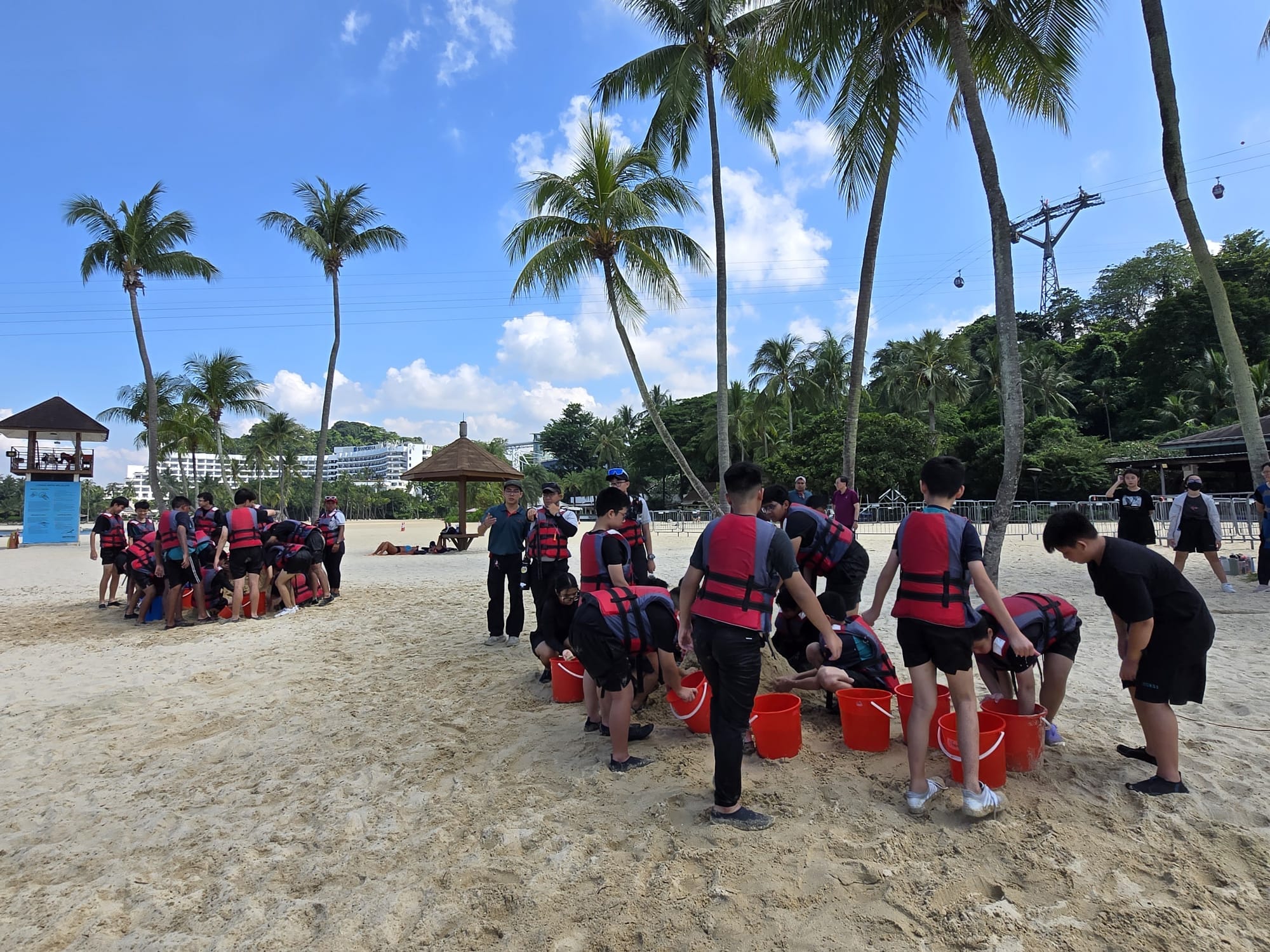 students standing around some pails on the beach