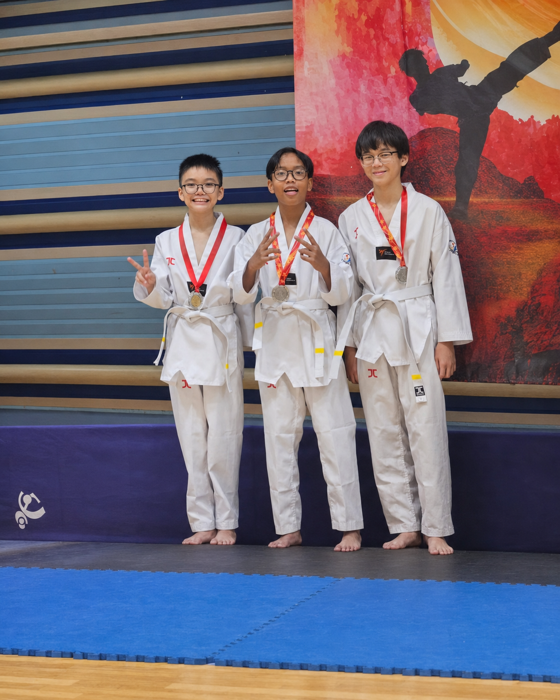 3 girls with a white belt in taekwondo stand on a podium with silver medals