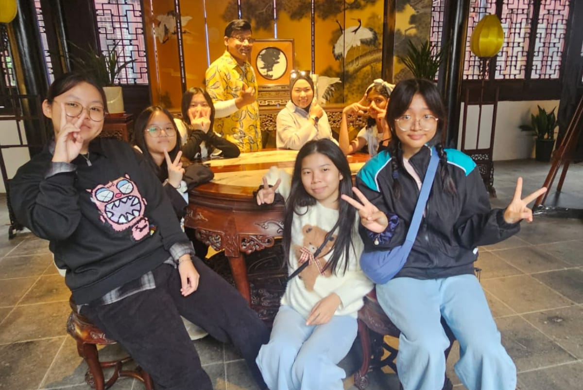 A group of young people pose with peace signs inside a traditional Chinese-style room with ornate wooden furniture.