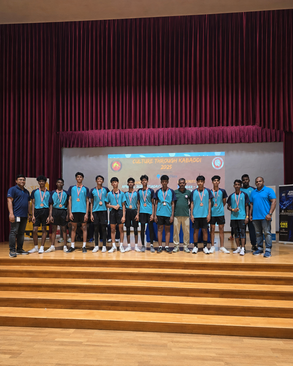A group of young athletes in teal jerseys wearing medals stand on a stage at Culture Through Kabaddi 2025.