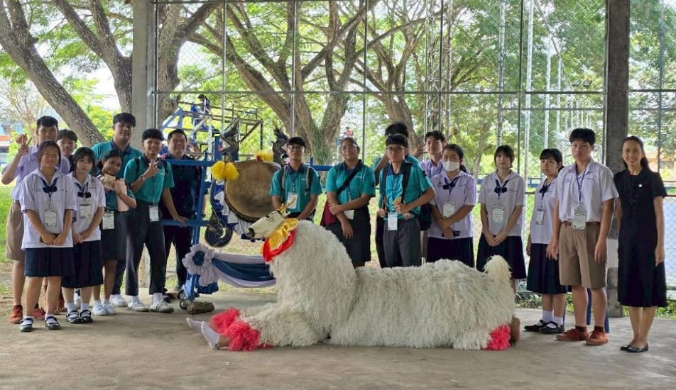 Group of students in uniforms posing with a decorated white fluffy animal costume and a large drum outdoors.