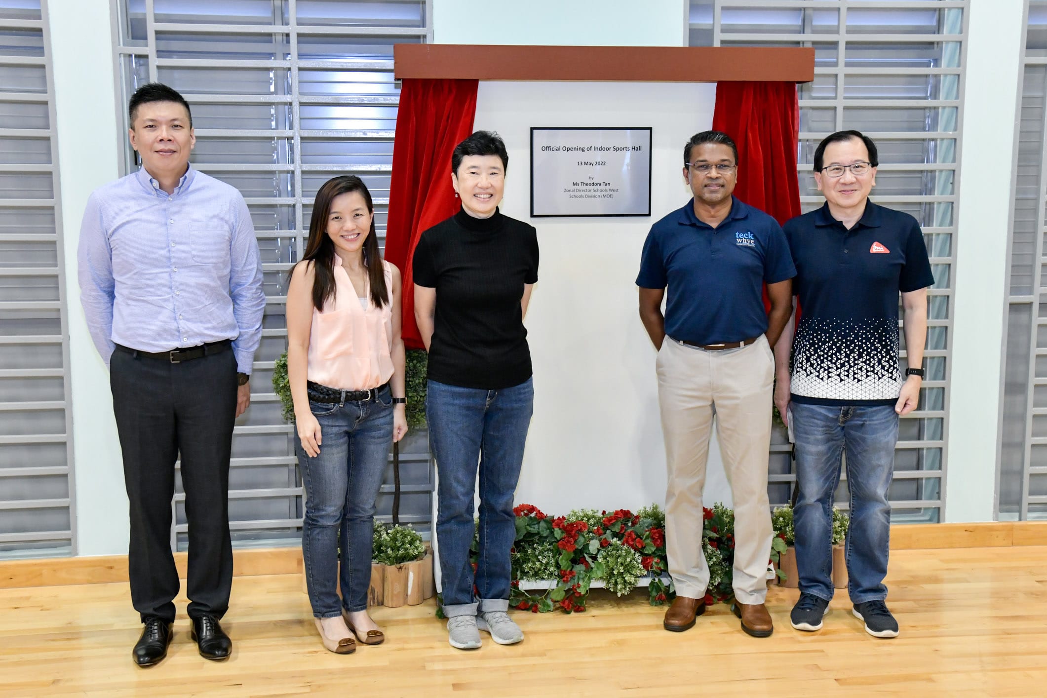 Five people stand smiling before a plaque reading Official Opening of Indoor Sports Hall, 13 May 2022.