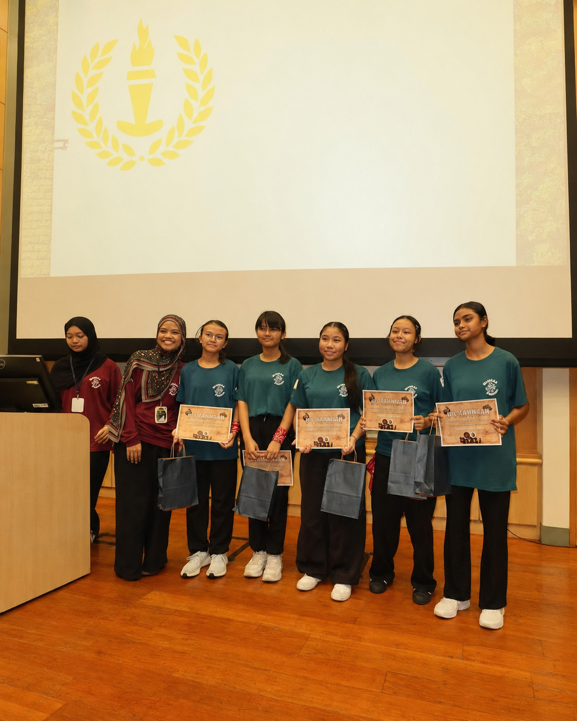 5 girls in green T-shirts stand next to two women wearing Hijab and red tops
