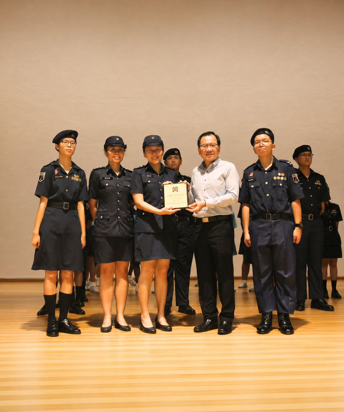 A group of teachers and cadets in NPCC uniform hand a plaque to the principal