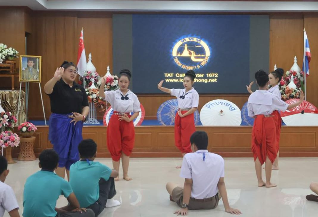 Young women in red pants perform a traditional Thai dance before seated students at a Tourism Authority of Thailand venue.
