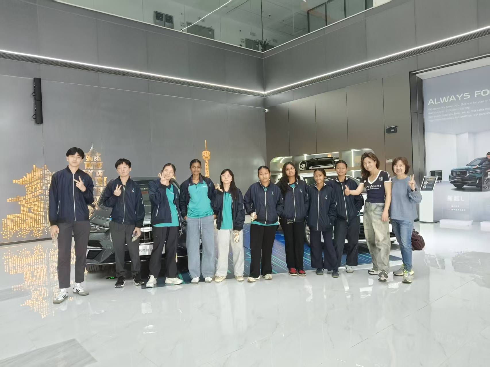 A group of about 12 students and adults pose in front of a dark car inside a modern car showroom.