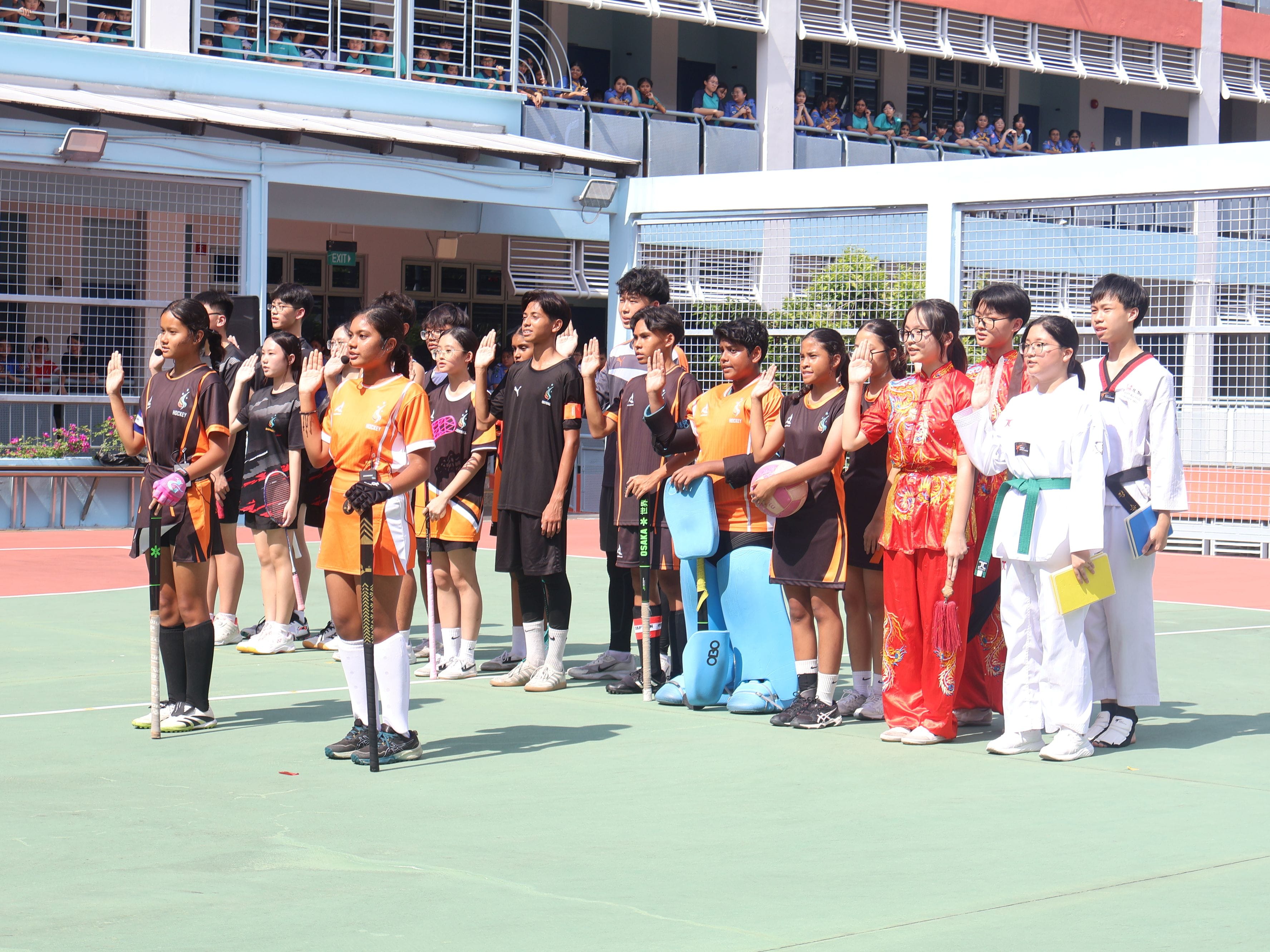 A group of students in sports attirue raise their right hands and take the pledge