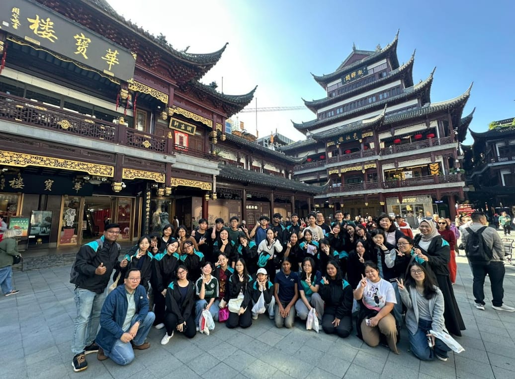 Large group of students in black and teal jackets posing in front of traditional Chinese architecture with gold signage.