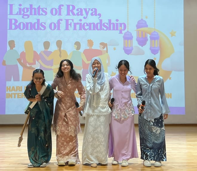 Five girls in traditional attire stand on stage at a Lights of Raya, Bonds of Friendship event, smiling together.