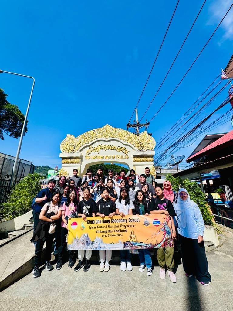 Group of students holding a Chua Chu Kang Secondary School banner at the Northernmost Point of Thailand arch.