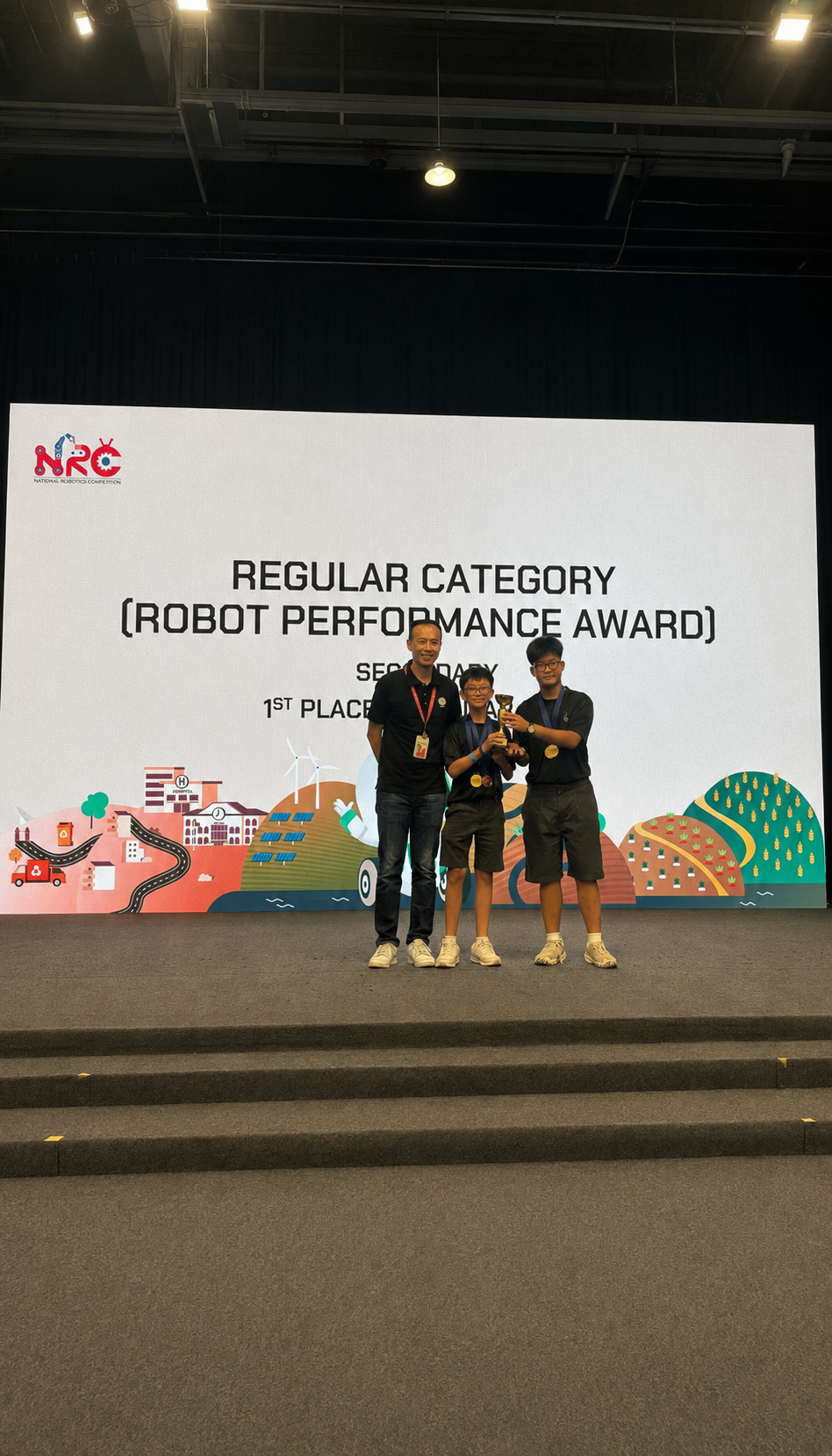 Three people stand on stage holding a trophy, in front of a screen reading Regular Category Robot Performance Award 1st Place.