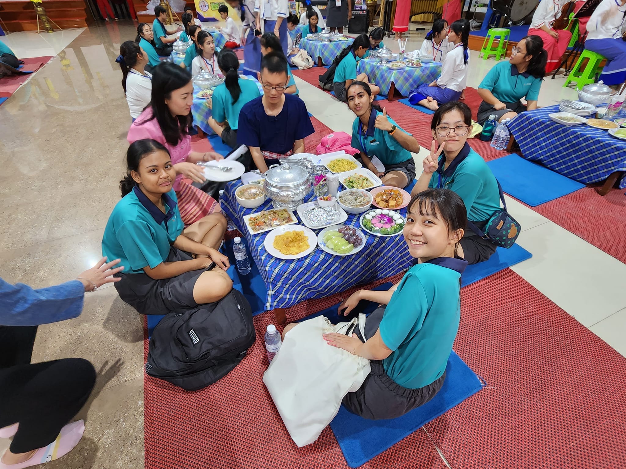 Students and teachers sitting on the floor for a meal.