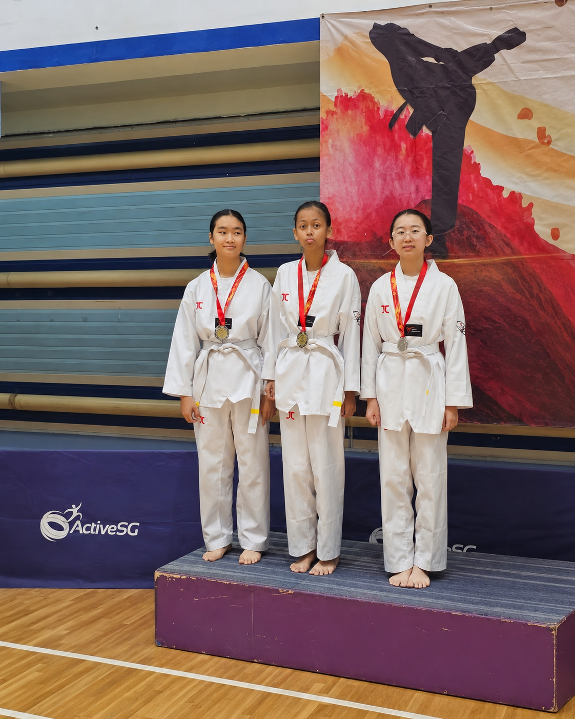 3 girls with a white belt in taekwondo stand on a podium with silver medals