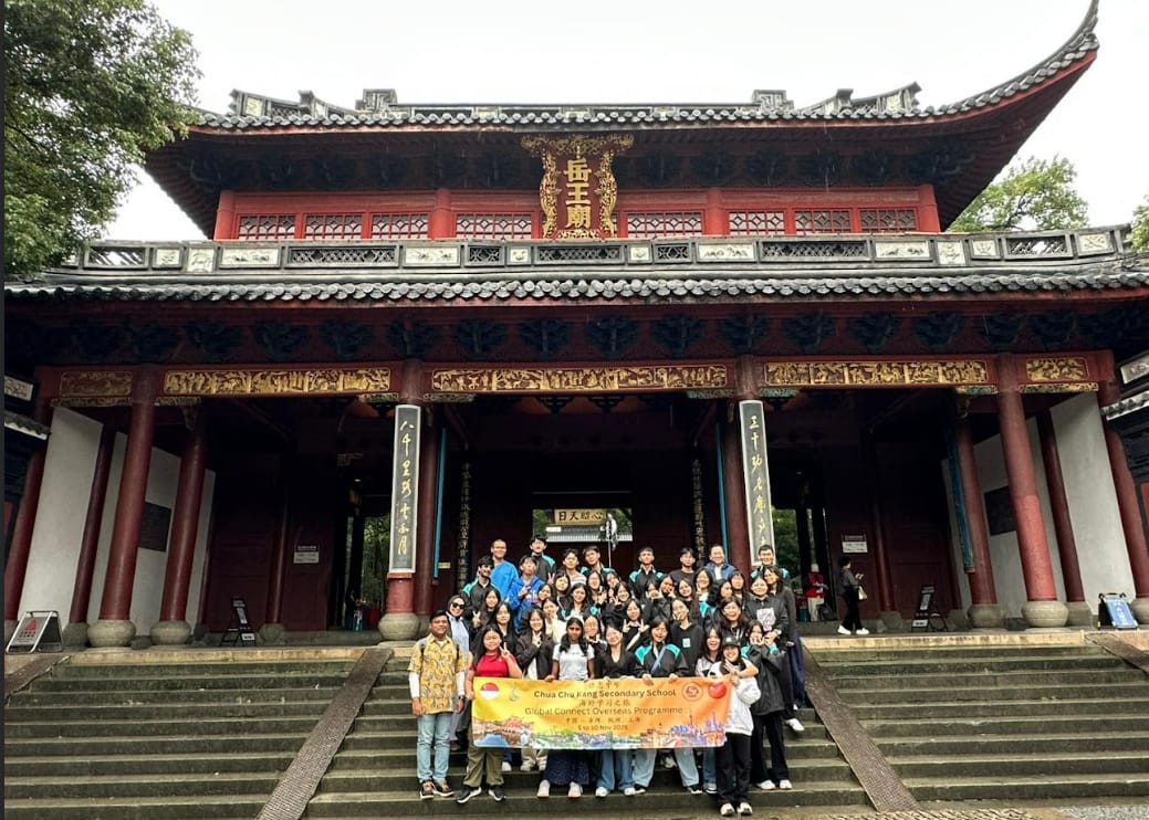 Group of students holding a Chua Chu Kang Secondary School banner on steps of a red Chinese temple.