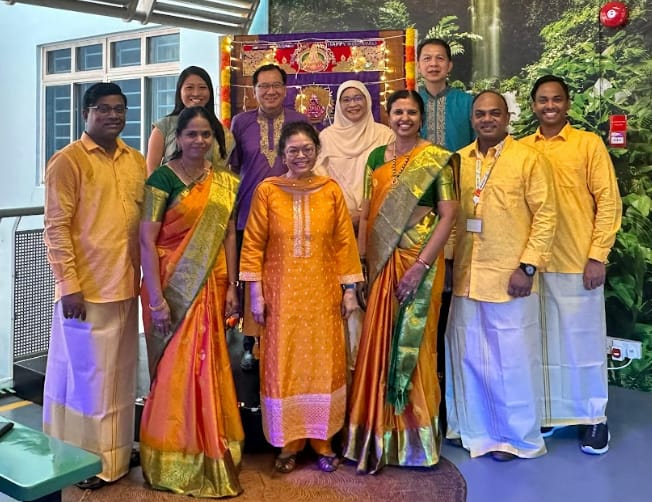 Ten people pose together wearing traditional Indian attire in orange and gold sarees and kurtas at a Diwali event.