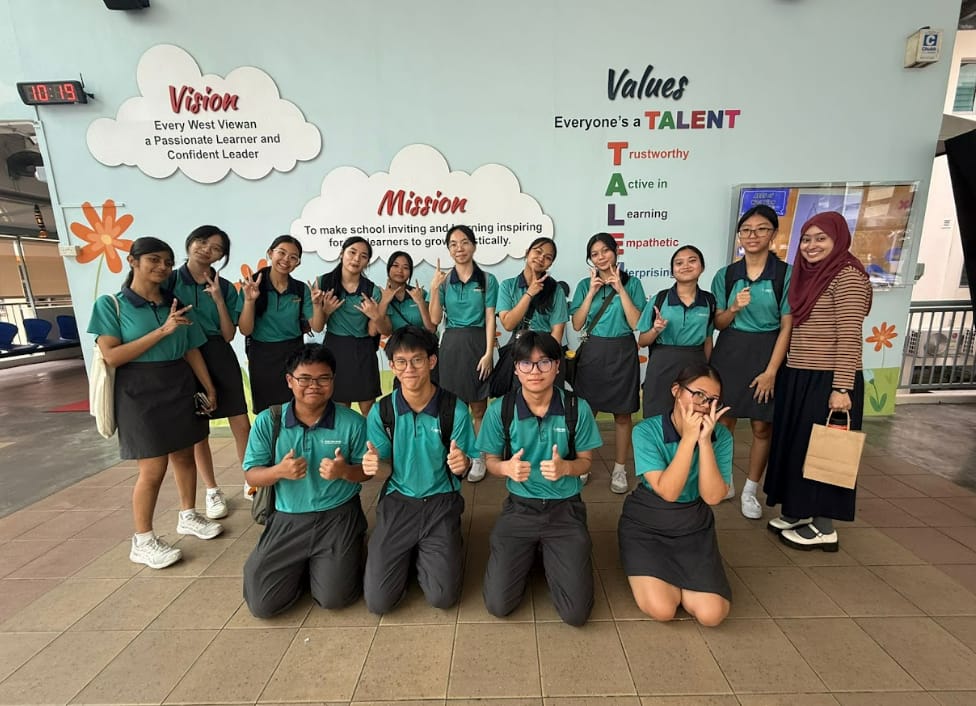 Students in teal uniforms pose in front of a school wall displaying Vision, Mission, and Values text.