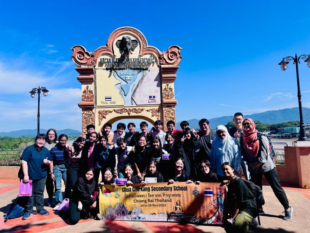 A school group poses with a banner at the Golden Triangle landmark in Chiang Rai, Thailand.